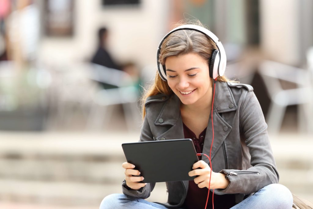 Une adolescente suit un cours en ligne dehors, à l'aide de sa tablette.