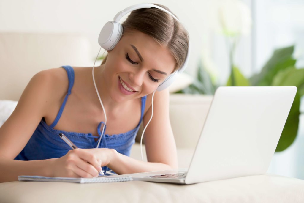 Élève souriante qui suit un cours d'été en ligne, à l'aide d'un ordinateur portable.