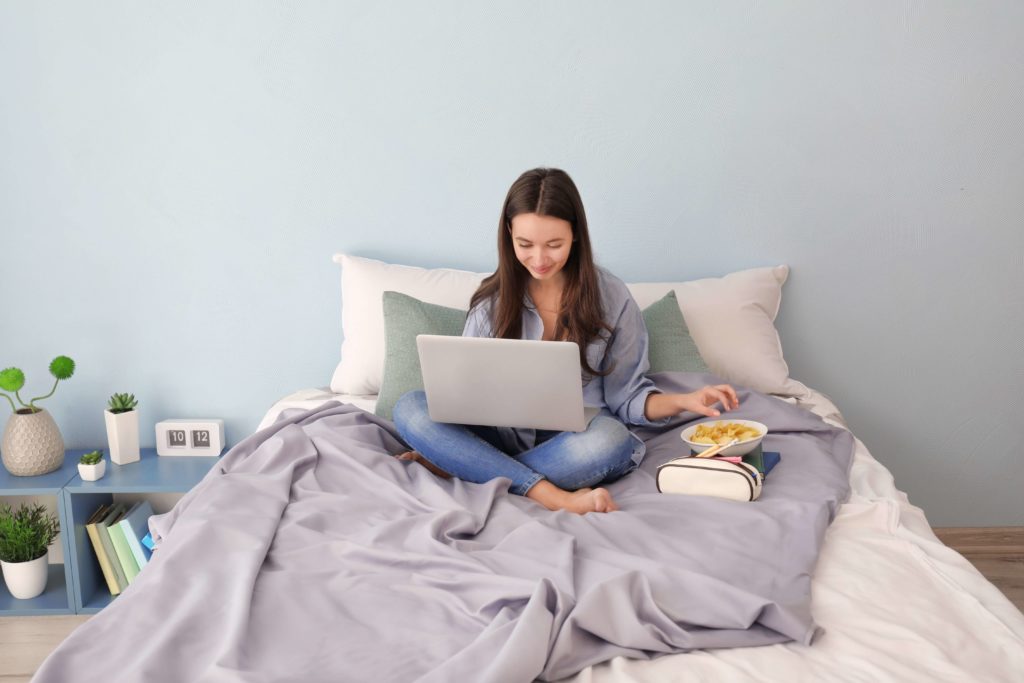 Une adolescente étudie pour son examen à l'ordinateur sur son lit.